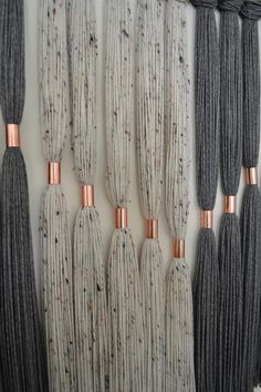 several different colors of yarn hanging on a wall with copper colored metal rods attached to them