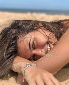 a woman laying in the sand with her arm around her head and hand on her chest