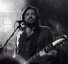 black and white photograph of a man playing guitar in front of a microphone on stage