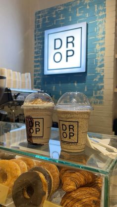 two cups of coffee sit on top of a counter with pastries and donuts