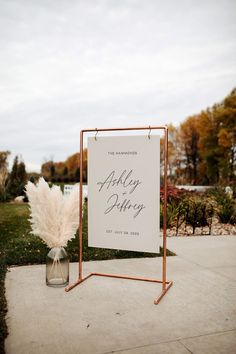 a sign that is on the side of a sidewalk next to some grass and flowers