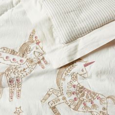 an embroidered bed spread with two horses on it's side and a striped pillow case in the background