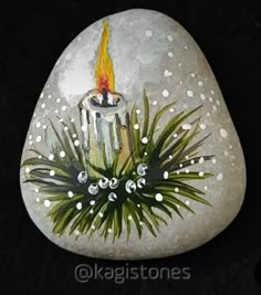 a painted rock with a lit candle and pine needles on it, surrounded by white dots