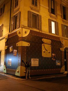 a man standing next to a giant suitcase on the side of a street at night