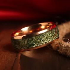 two gold wedding bands with green moss on them sitting next to a piece of rope