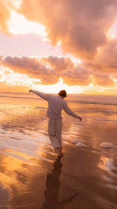 a man is walking on the beach at sunset