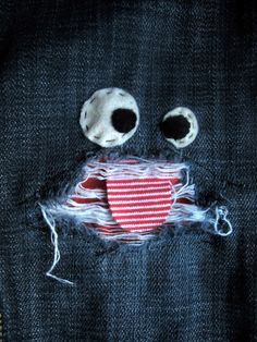 a piece of cloth with two eyes and a red heart in the middle, sitting on top of a blue jean jacket