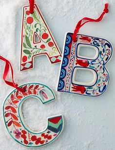 three christmas ornaments are hanging on the snow covered ground, one is decorated with flowers and the other has a letter shaped ornament