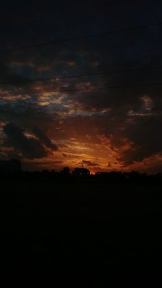 the sun is setting behind some clouds in the sky over an open field with power lines