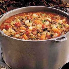 a pot filled with stew sitting on top of a stove next to some bread and vegetables