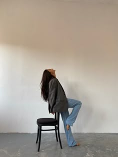 a woman sitting on top of a chair in front of a wall with her back to the camera