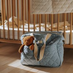 a teddy bear in a blue quilted bag next to a crib