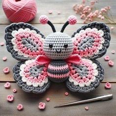 a crocheted butterfly sitting on top of a wooden table next to yarn and knitting needles