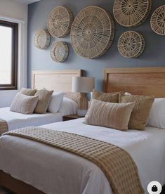 two beds in a room with wicker baskets on the wall above them and windows