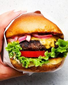 a hamburger with lettuce, tomato and cheese on it is being held by someone