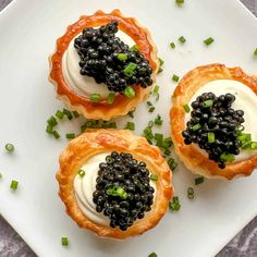 three small tarts with blackberries and cream on top are sitting on a white plate