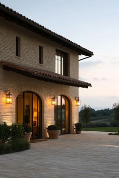 an outside view of a house with lights on and potted plants next to it