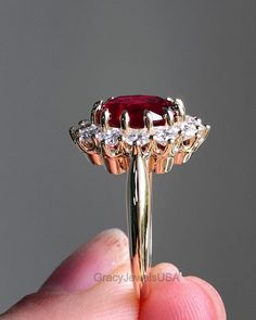 a close up of a person's hand holding a ring with a red stone