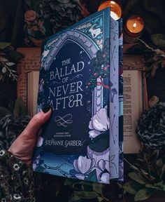 a person holding up a book in front of some flowers and candles with the title, the ball of never after