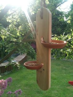 a bird feeder hanging from the side of a tree in a yard with flowers around it