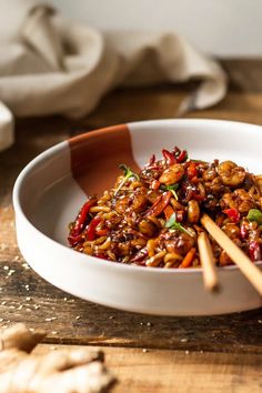 a white bowl filled with stir fry and chopsticks on top of a wooden table