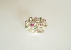 My rose bouquet consists of two larger roses, three medium roses and five buds. Five faceted rubies sparkle in the open flowers. Small transparent green enameled leaves surround the bouquet. The ring band appears to be wrapped from the rose stems. I modeled this unique piece in wax and had it cast in recycled 925 silver (lost shape). The rose bouquet has a ring width of 56 and can be brought to a width of 57. The bouquet of roses, which never withers, is delivered in a nice black jewelry box. Elegant Silver Rings With Rose Details, Elegant Sterling Silver Rings With Roses, Fine Jewelry Rose Design Ring, Wedding Jewelry With Roses In Sterling Silver, Wedding Jewelry In Sterling Silver With Roses, Rose Red Roses Wedding Jewelry, Rose Red Roses Jewelry For Weddings, Rose Jewelry With 3d Flowers For Gift, Red Rose Jewelry For Anniversary