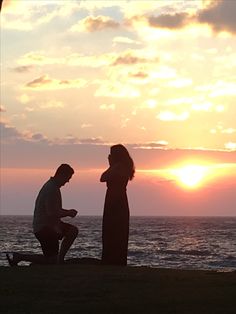 two people are standing on the shore watching the sun go down over the ocean with clouds in the sky