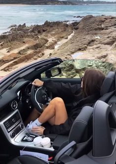 a woman sitting in the driver's seat of a car next to the ocean