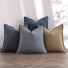 three pillows sitting on top of a wooden floor next to a white wall and window