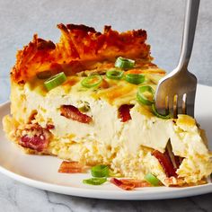 a piece of quiche on a white plate with a fork in it and green onions