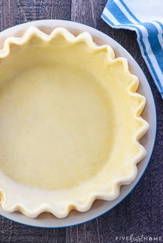 a pie crust in a blue and white dish on top of a wooden table next to a striped napkin