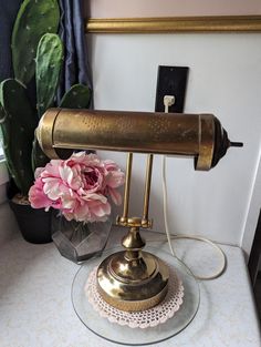 a brass table lamp sitting on top of a white table next to a potted plant