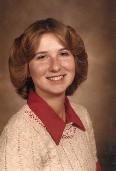 an old photo of a woman in a sweater smiling at the camera and wearing a red collared shirt