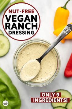 a spoon in a jar filled with ranch dressing next to sliced cucumbers and peppers