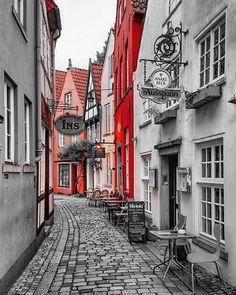 an old cobblestone street with tables and chairs on the side in front of red buildings