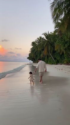 a man and child are walking on the beach at sunset with palm trees in the background