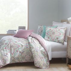 a white bed with pink and green pillows on top of it next to a window