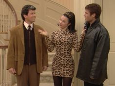 two men and a woman standing next to each other in front of a stair case