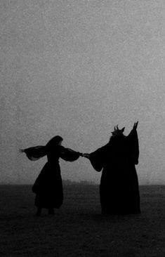 two women in long dresses are holding hands and flying kites on a foggy day