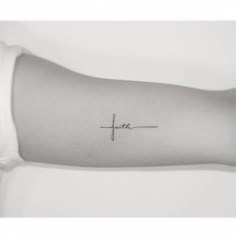 a small cross tattoo on the arm that says faith in cursive writing,