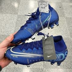 a hand holding a pair of blue nike soccer cleats with a price tag on it
