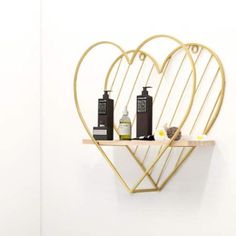 a gold heart shaped shelf with two bottles on it and soaps in the middle