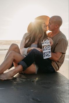 a man and woman are sitting on the beach with their arms around each other as they kiss