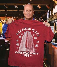 a man holding up a t - shirt that says nakatami plaza christmas party