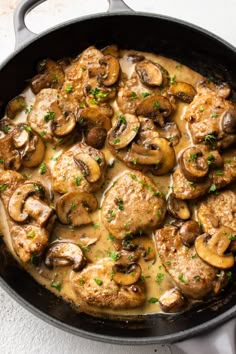 a skillet filled with chicken, mushrooms and gravy on top of a white table