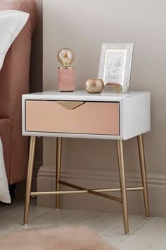 a pink and white nightstand next to a bed with a framed photograph on top of it