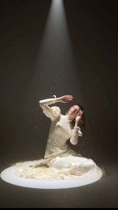 a woman in white dress sitting on top of a pile of shredded up paper under a spotlight