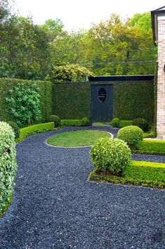 an outdoor garden with hedges and gravel path leading to a gate in the center, surrounded by shrubbery