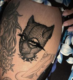 a woman's thigh with tattoos on it and an image of a cat in the background