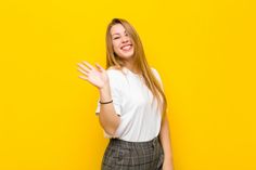 a woman standing in front of a yellow wall holding her hands out to the side